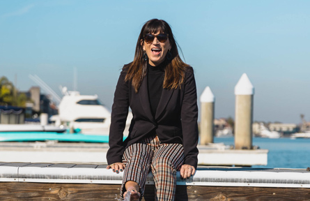 Girl with suit and pants and sunglasses sitting by the dock in morning
